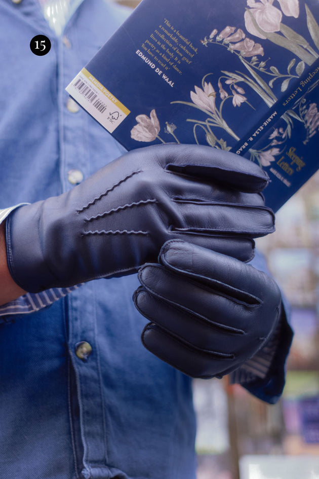 Man wearing blue leather gloves in navy holding a book