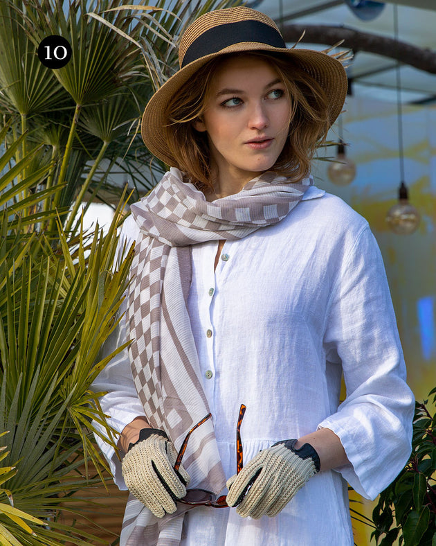 Woman wearing crochet back leather driving gloves in black with a check scarf and straw hat on holiday