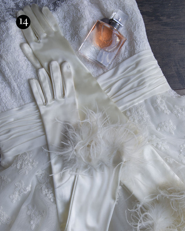 Womens long satin gloves with feathered cuffs in white laid out on a wedding dress