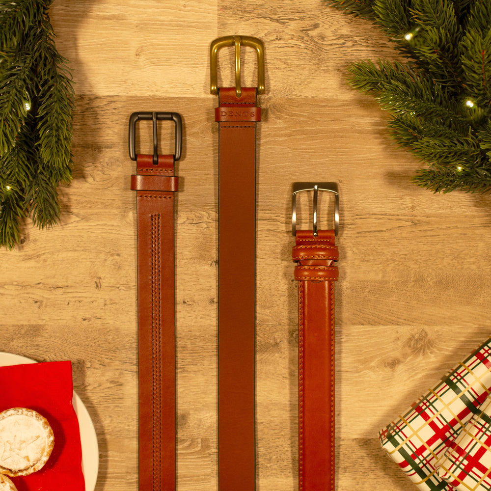 Selection of men's brown leather belts on a wooden table with Christmas accessories