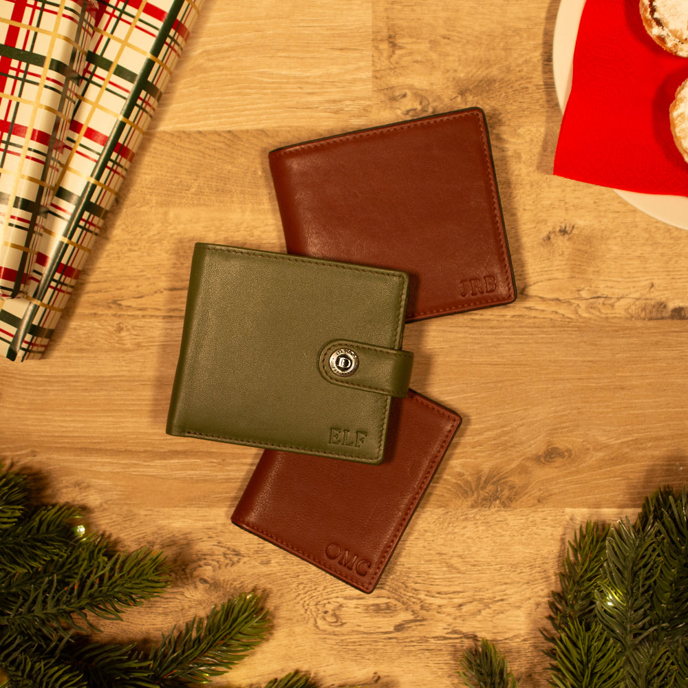 Selection of brown and green men's leather wallets with debossed initials on a wooden table