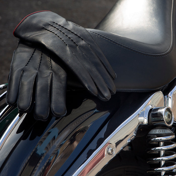 Men's black leather gloves with red lining laid on a motorcycle