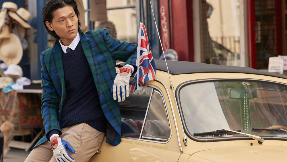 Man wearing multi-coloured crochet-back leather driving gloves stood next to a car with a union jack flag in the city