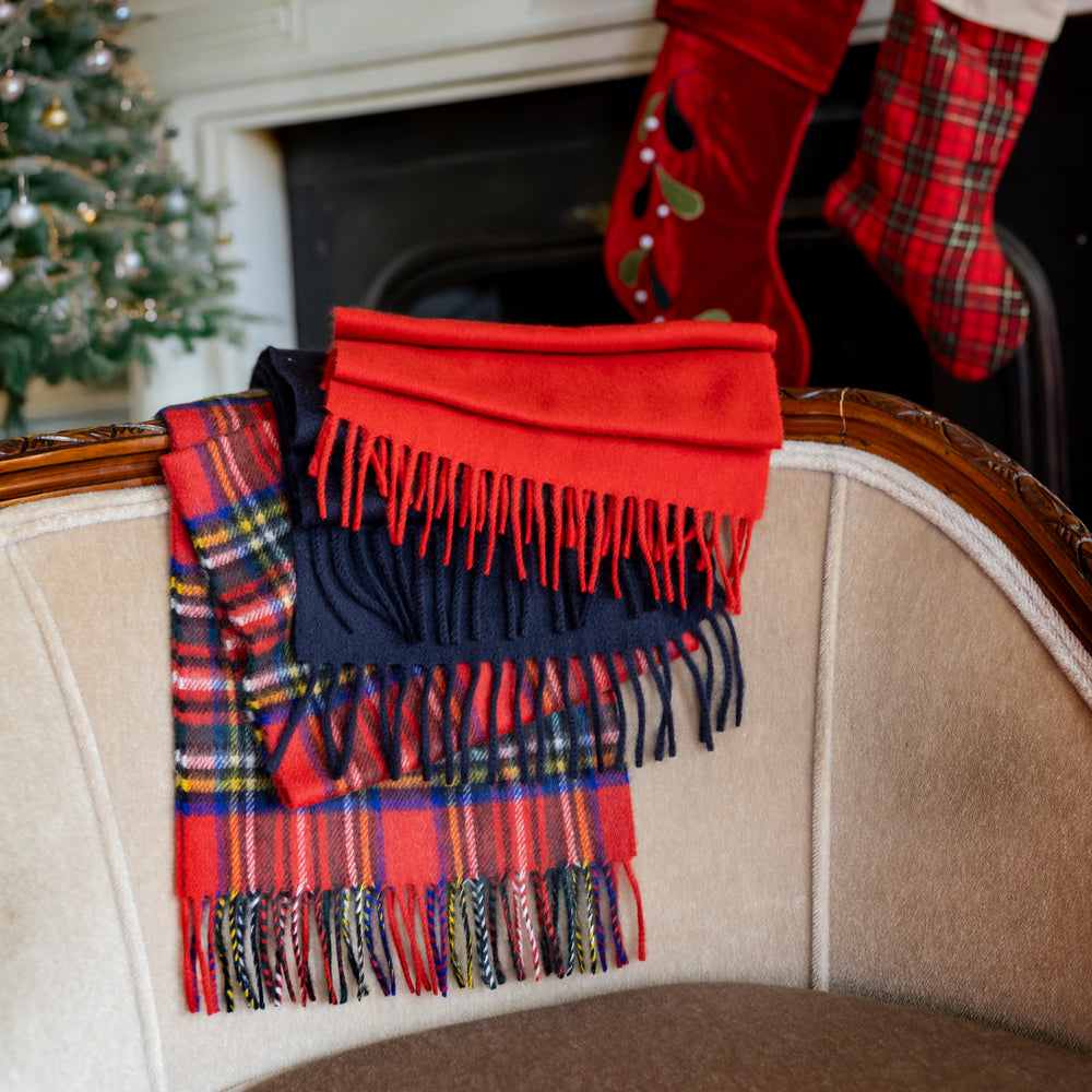 Three cashmere scarves in different colours and designs draped over a cream sofa with a festive background