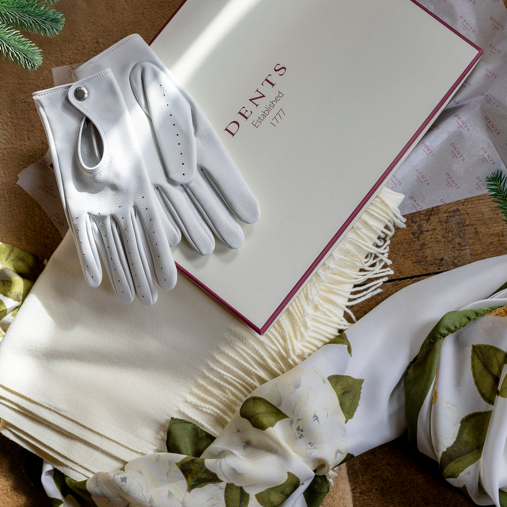 Women's leather driving gloves, pashmina shawl and floral silk-like scarf with a gift box against a festive background
