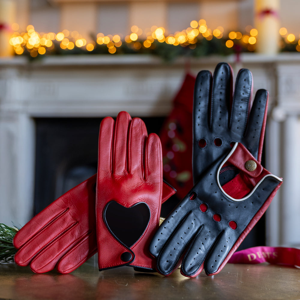 Men's and women's black and red leather driving gloves on a table with a festive background