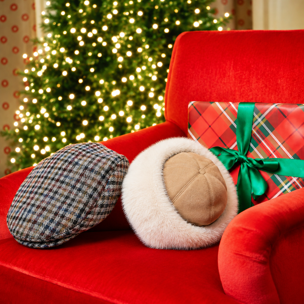 A men's checked tweed flat cap and a women's faux fur-trimmed suede hat on a red armchair in front of a Christmas tree