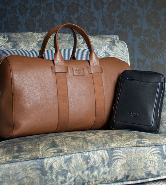Men's leather bags in black and caramel on a blue floral sofa