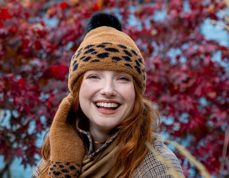 Woman wearing spotty feather yarn hat in tan, with matching gloves, outside. 