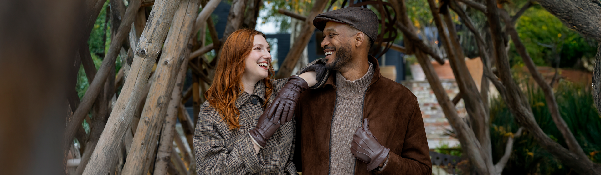 Man and woman wearing brown leather gloves with three-point, together by the trees.