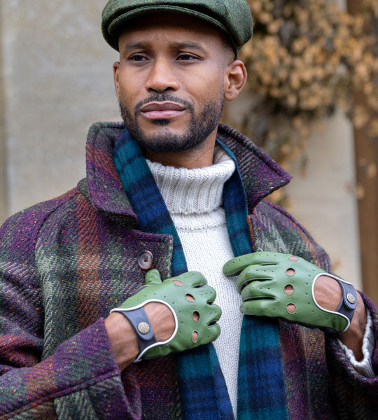 Man wearing three-colour leather driving gloves in green with scarf and hat outside. 