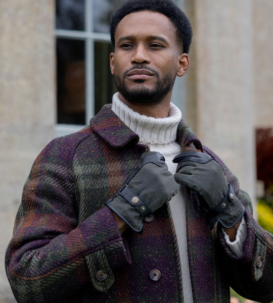 man wearing leather and water-resistant gloves in green in a big coat, outside in the garden. 