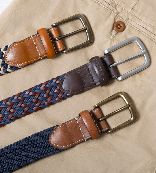 Men's leather belts in various colours laid out on  a pair of linen trousers