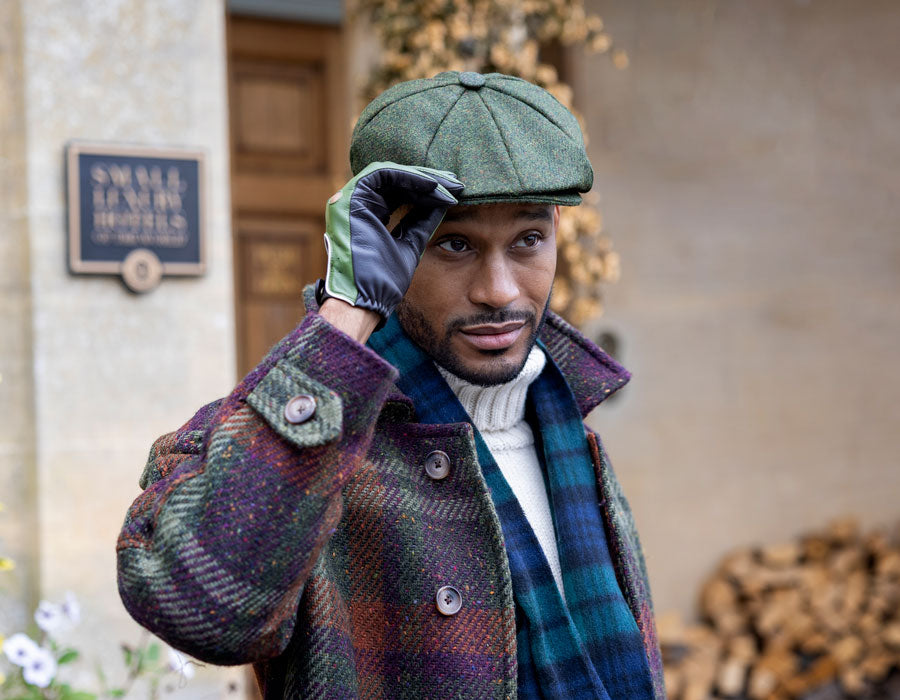 Man wearing a tweed cap in green with driving gloves and scarf outdoors