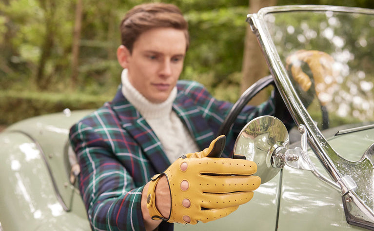 Man wearing leather driving gloves in yellow sitting in a classic car