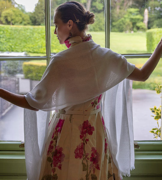Woman wearing silver summer scarf with an evening dress standing by the window of a manor house