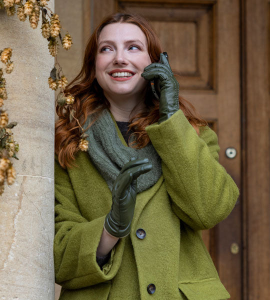 Woman wearing touchscreen leather gloves in sage using her mobile phone outside of a state home