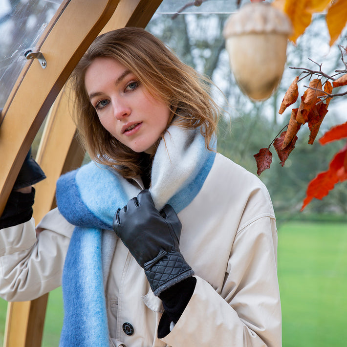 Woman wearing grey leather gloves and blue blanket scarf at an outdoor cafe in autumn