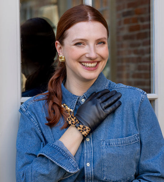 woman wearing leather gloves with animal print bow next to a doorframe. 