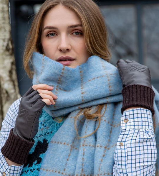 Woman wearing blue blanket scarf with tassels outside. 
