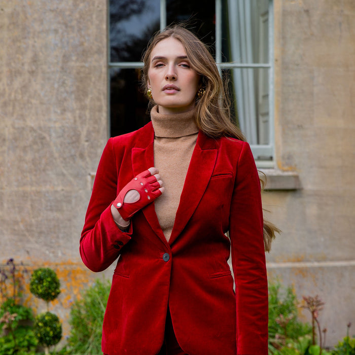 Woman wearing fingerless leather driving gloves in berry with a red jacket