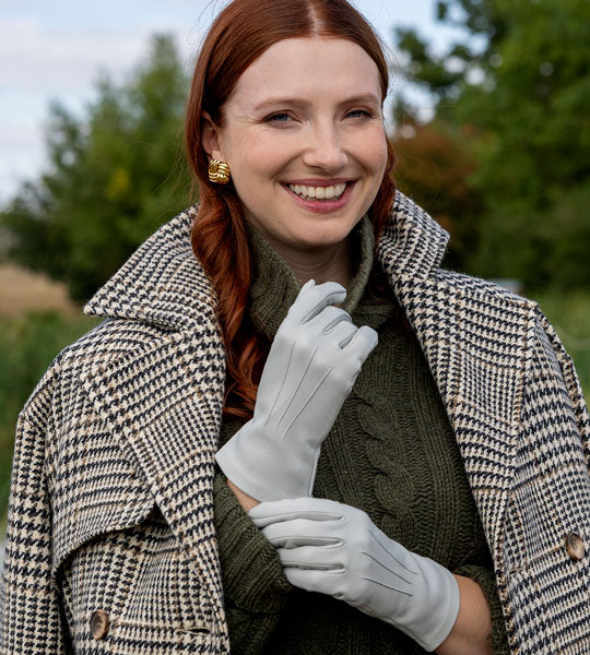 Woman wearing three-point leather gloves in light grey with winter coat. 