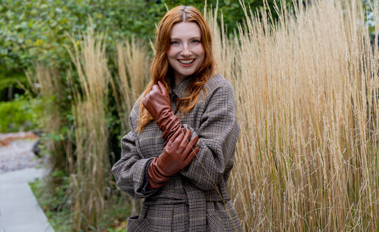 Woman wearing long, above elbow, single-point leather gloves in brown standing outside.