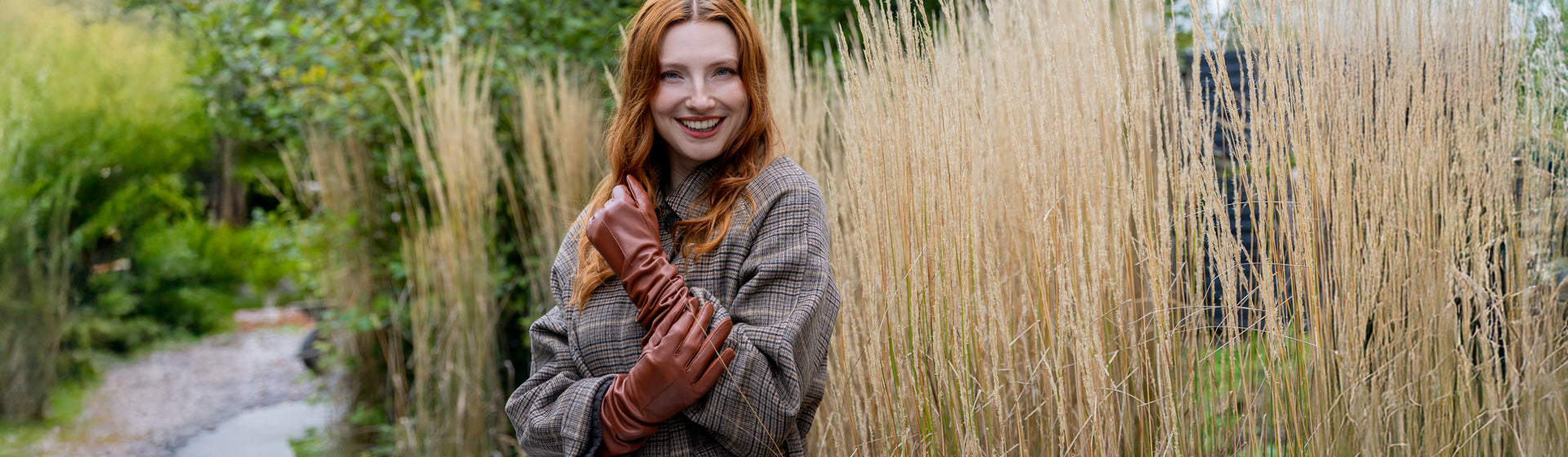 Woman wearing long, above elbow, single-point leather gloves in brown standing outside.