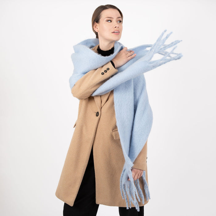 Woman wearing a blanket scarf with tassels in pale blue thrown over her shoulder