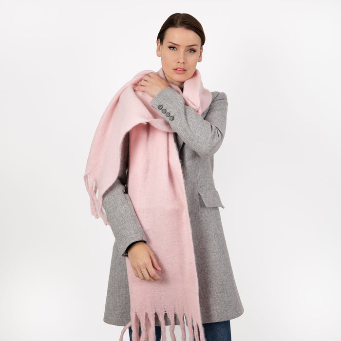 Woman wearing blanket scarf with tassels in pale pink thrown over her shoulder