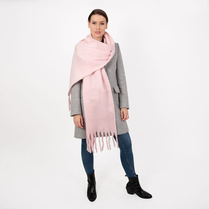 Woman wearing blanket scarf with tassels in pale pink thrown over her shoulder
