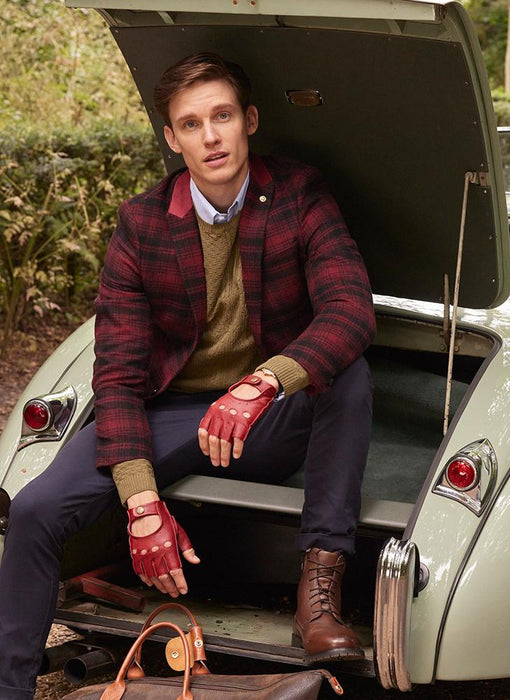 Man wearing berry fingerless leather driving gloves sitting in a car in the forest