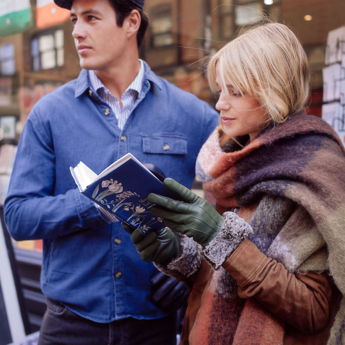 Man and woman standing reading a book. Woman is wearing checked scarf and sage leather gloves with faux fur cuffs.