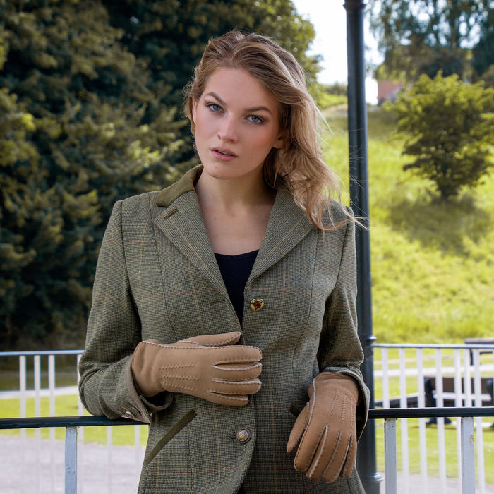 Woman stood by railings in a park, wearing light brown lambskin gloves.