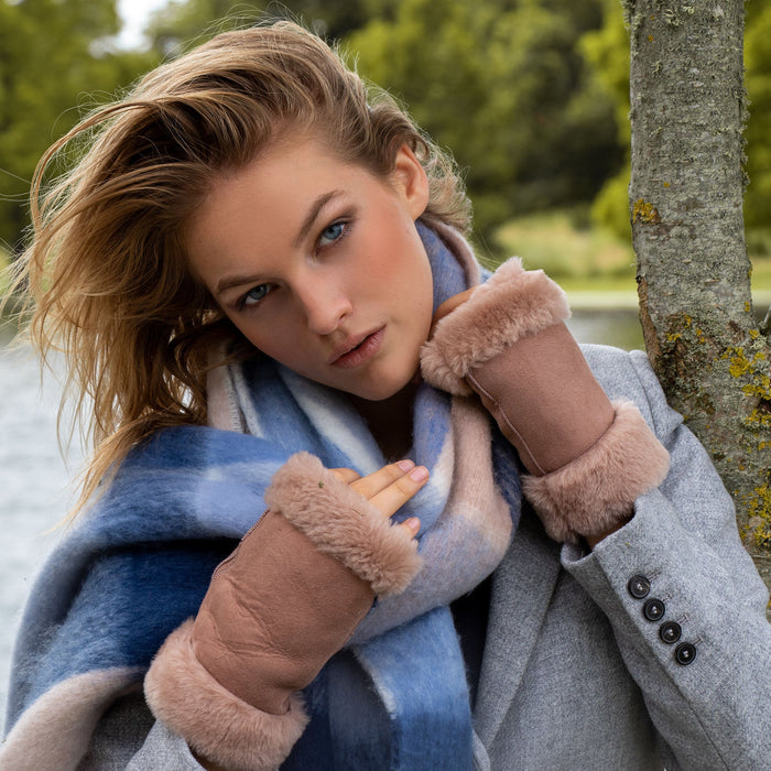 Woman standing in front of a tree in a park wearing light brown fingerless mittens, with sheepskin fur.