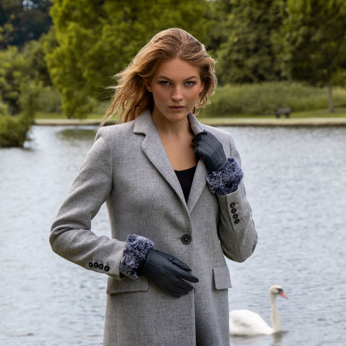 Woman standing in front of a lake, wearing navy leather gloves with a faux fur cuff.